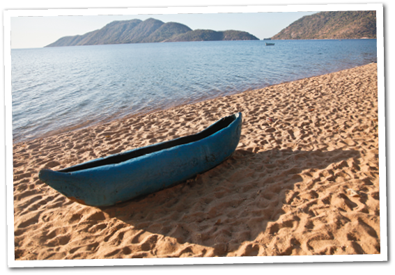 Blue Canoe on the lake shore of Lake Malawi in Malawi  The deserted lake shore remains peaceful in the evening sun  This canoe was left abandoned on the warm sand as the sun set 
